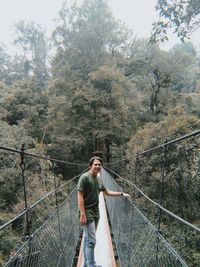 Young man standing on footbridge in forest