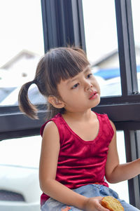 Cute girl looking away while sitting on window