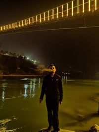 Full length of man smoking cigarette standing by river against sky at night