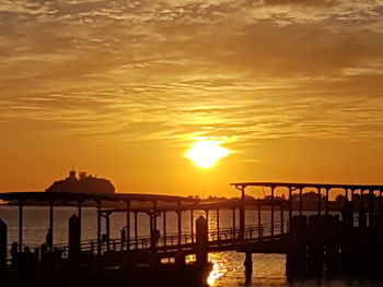 Silhouette pier over sea against orange sky