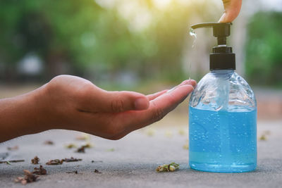 Close-up of hand holding bottle against water