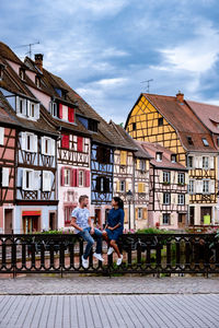 People sitting by building in city against sky