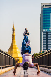 Rear view of man walking on bridge against buildings in city