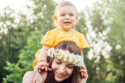 Woman carrying baby on shoulders against plants