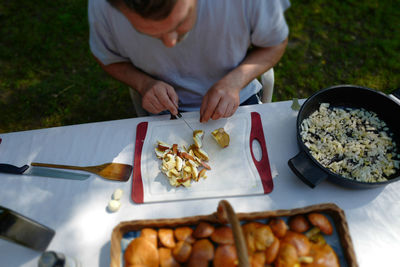 High angle view of man cutting mushroom while sitting at table in yard