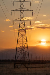 Low angle view of electricity pylon on field against sky during sunset