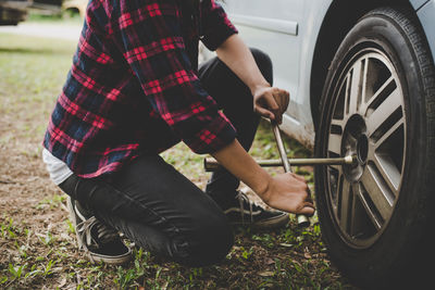 Low section of woman removing tire of car on field