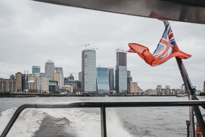 Canary wharf skyscrapers from thames clippers boat on river thames, british naval flag on the mast.