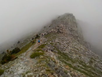 Person climbing on mountain against sky during foggy weather