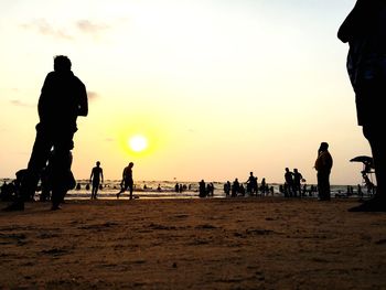 Silhouette people on beach against sky during sunset