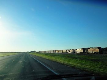 Road amidst field against clear blue sky