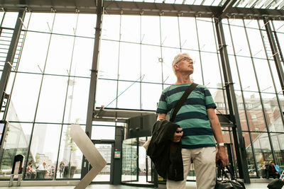 Low angle view of senior man with luggage standing at railroad station