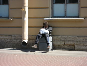 Rear view of man sitting on footpath against building