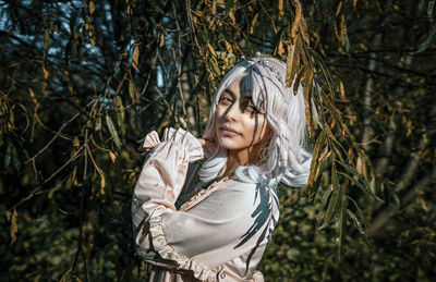 Young woman standing by tree in forest