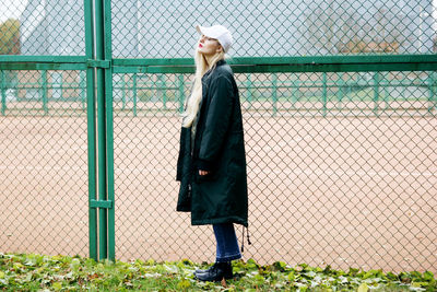 Side view of woman standing by chainlink fence on field