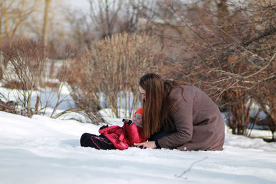 Side view of woman sitting on snow covered landscape