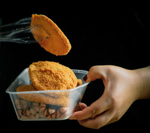 Close-up of hand holding ice cream against black background