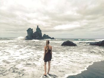 Woman standing on rock at beach against sky