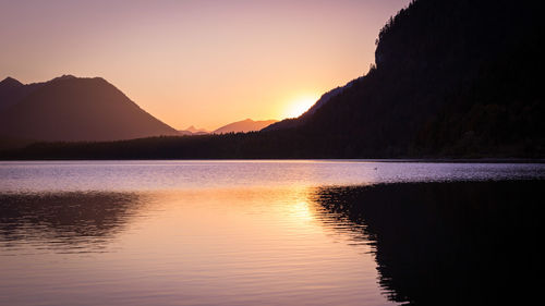 Scenic view of lake by silhouette mountains against sky during sunset