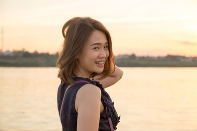 Portrait of smiling young woman standing against sea and sky during sunset