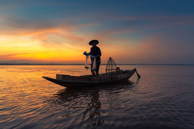 Silhouette fisherman holding fishing net in boat on sea during sunset