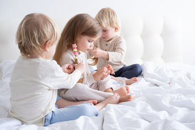 Siblings braiding hair of sister on bed at home