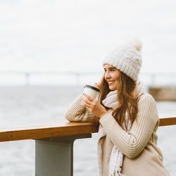 Young woman holding coffee while standing outdoors during winter