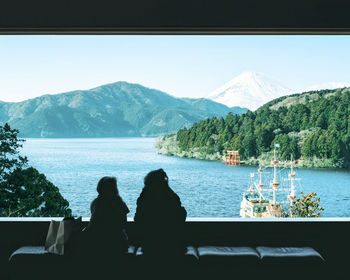 People sitting on lake against mountains