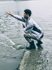 Man crouching on pier against sea