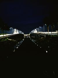 Illuminated footbridge over city against sky at night
