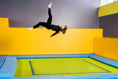 Full length of man jumping against yellow wall