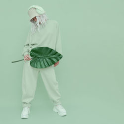 Full length of woman holding leaf while standing over green background