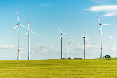 Windmills on grassy field against sky