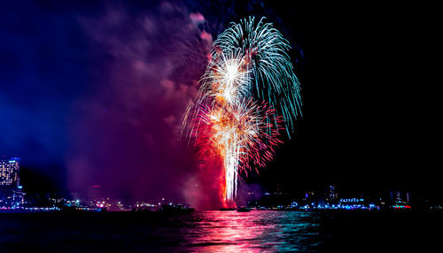 Firework display over illuminated cityscape against sky at night