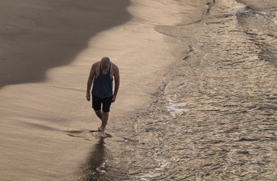 Adult man walking on a beach with ocean wave during sunrise