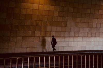 Rear view of man walking against brick wall