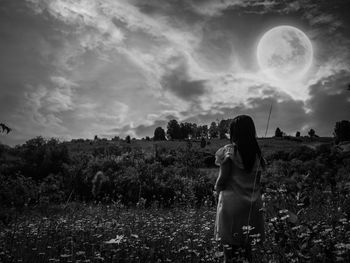 Rear view of woman photographing on field against sky