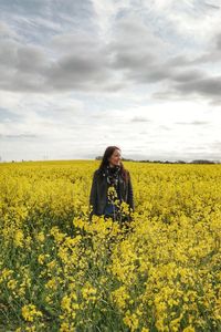 Woman standing in rapeseed field against cloudy sky