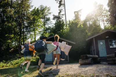 Rear view of happy kids running towards cabins at summer camp