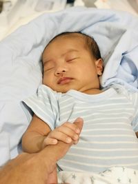 High angle view of baby boy sleeping on bed at home holding a finger