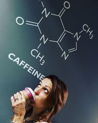 Portrait of a young woman drinking caffeinated drink in front of chemical structure of caffeine