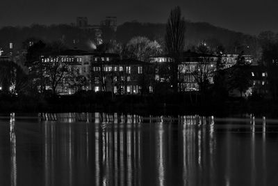 Illuminated building by lake against sky at night