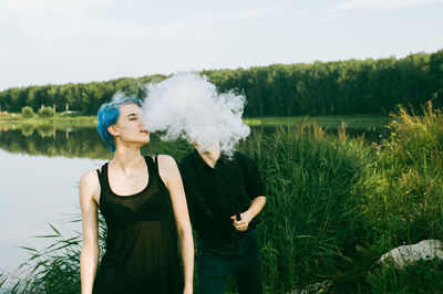 Friends smoking electronic cigarette at lakeshore