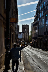 Rear view of man walking on railroad tracks amidst buildings in city