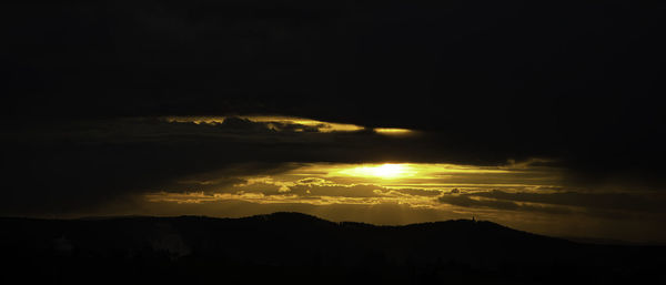 Scenic view of silhouette mountain against dramatic sky during sunset