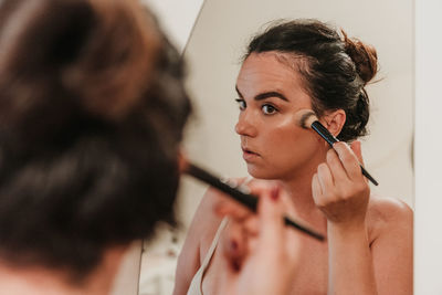 Mirror photo of beautiful young woman putting on makeup