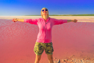 Woman with arms outstretched standing by pink lake