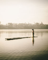 Fisherman standing in boat against sky