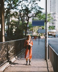 Portrait of young woman holding railing against bridge in city