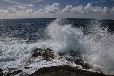 Waves splashing on rocks against sky